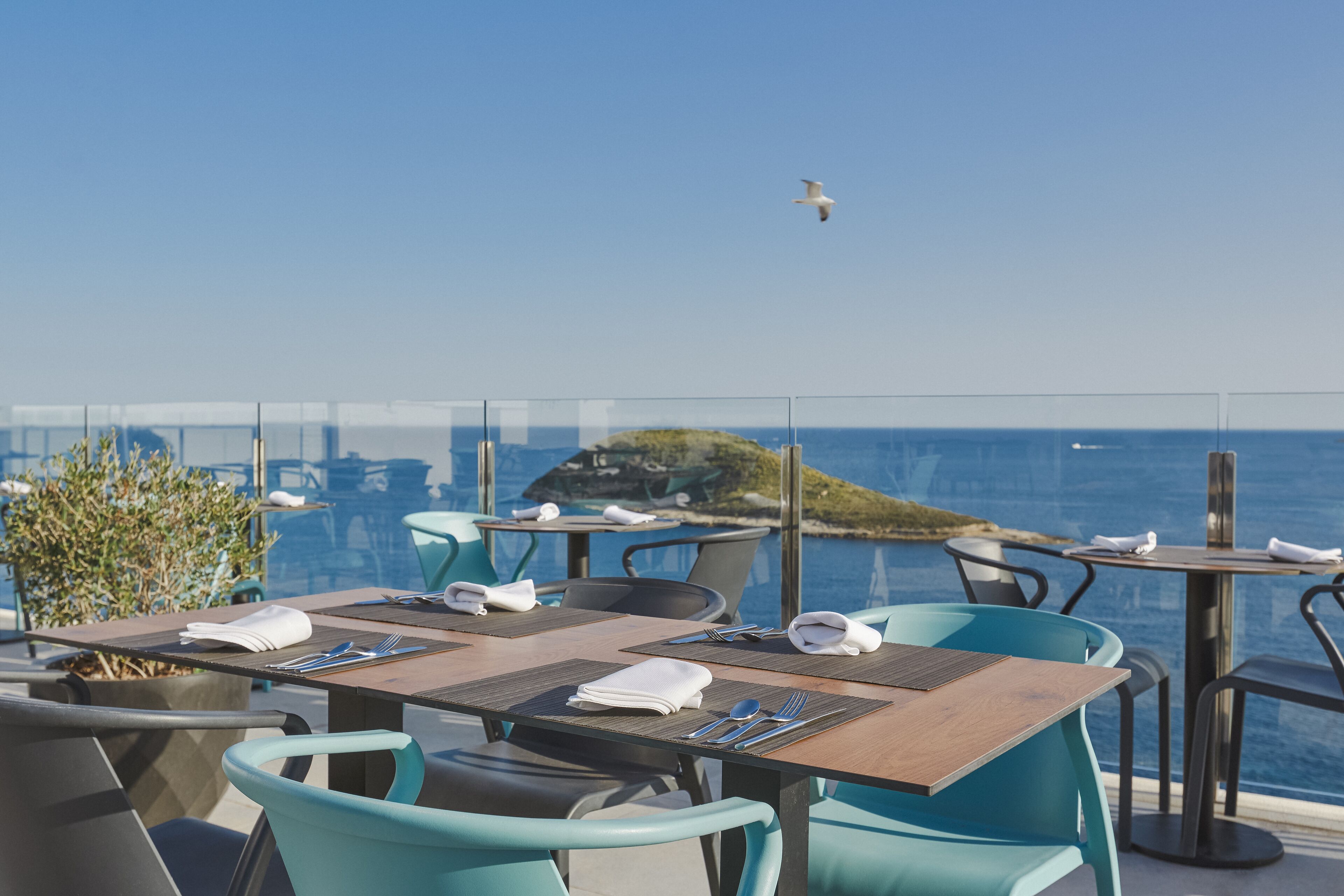 Un comedor con mesas y sillas, con vistas a una masa de agua y una costa lejana.