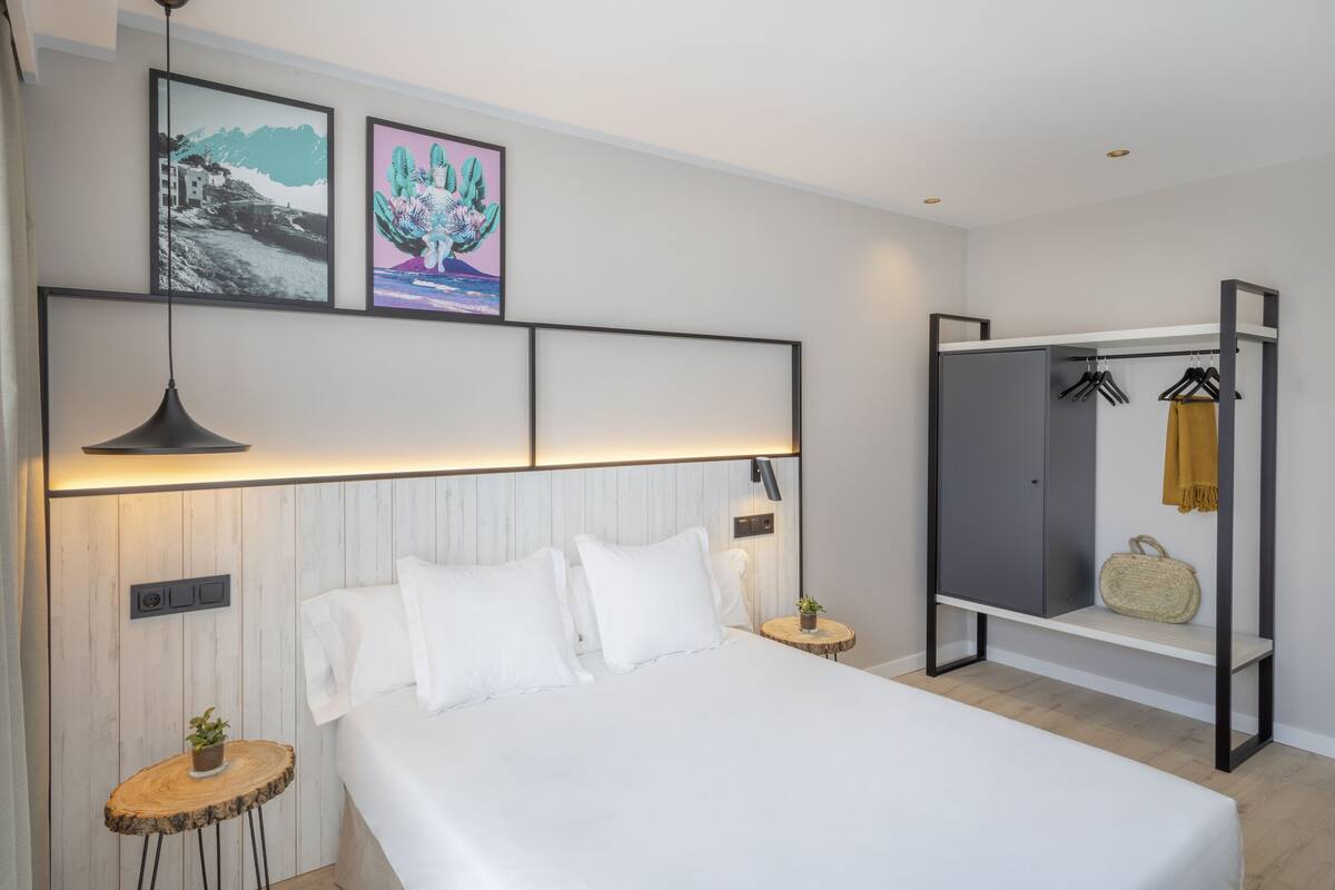 Une chambre moderne avec un grand lit, des tables de chevet, une armoire et des œuvres d’art accrochées au mur.