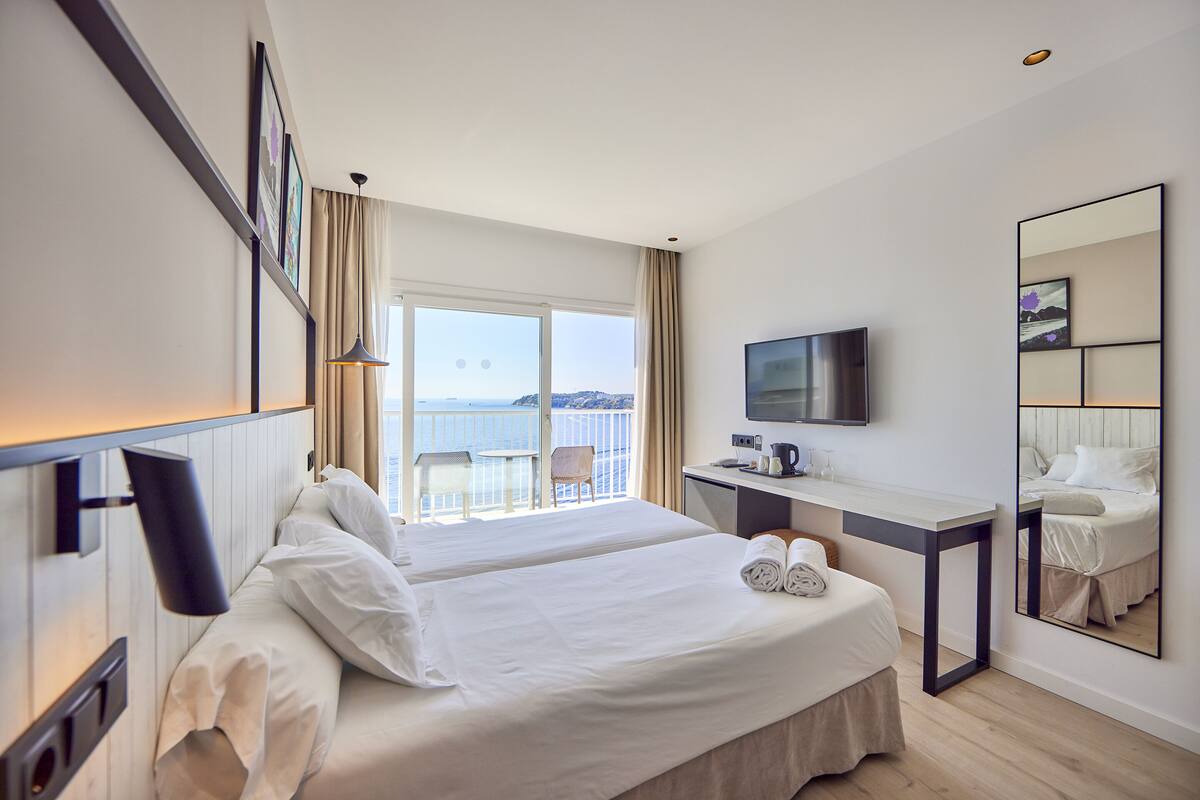 Une chambre d’hôtel avec un grand lit, un bureau, une télévision et un balcon donnant sur la mer.