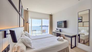A hotel room with a large bed, a desk, a TV, and a balcony with a view of the sea.