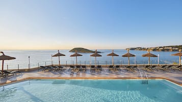 Una piscina al aire libre, sombrillas, sillones reclinables de piscina