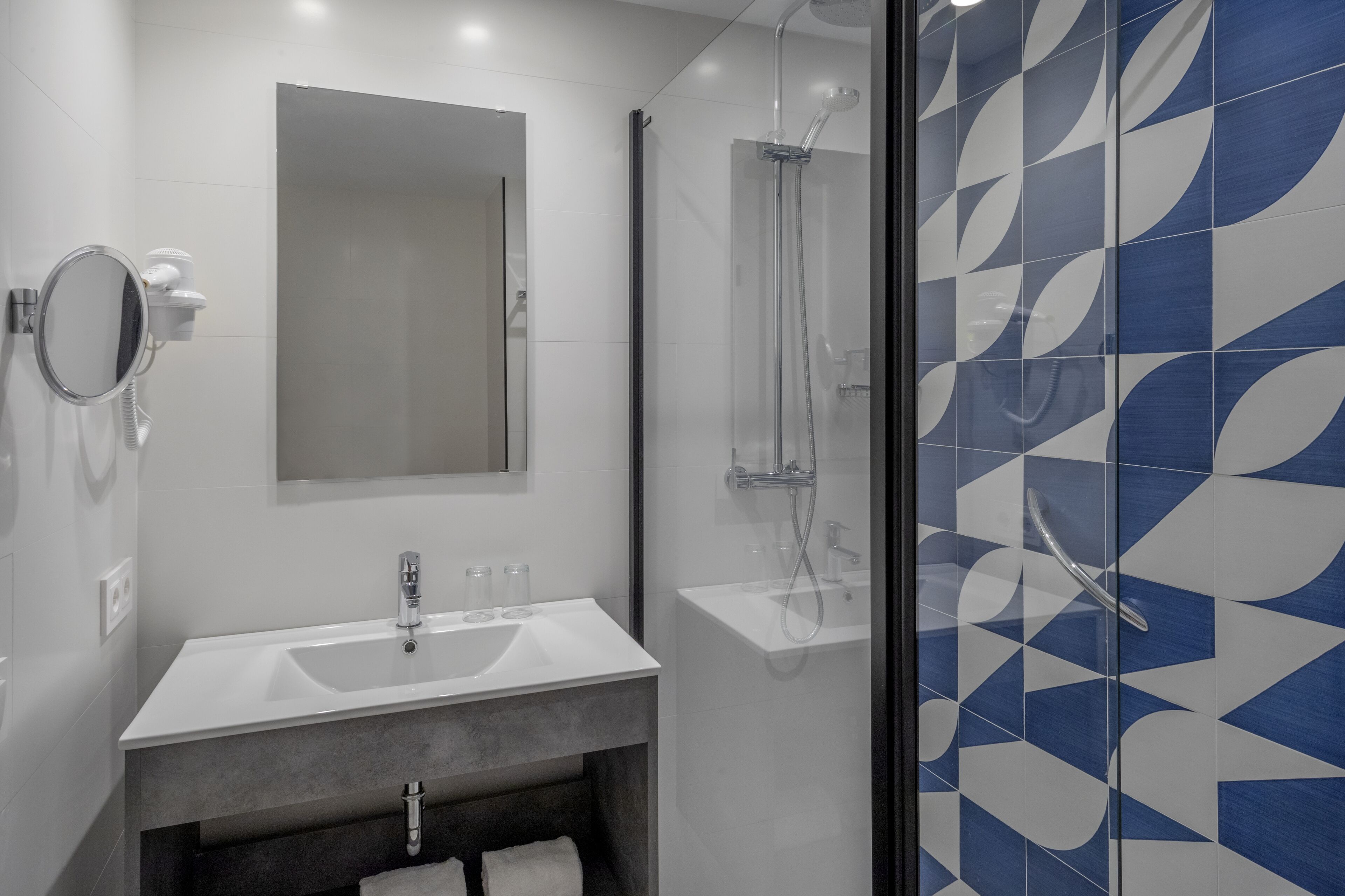 Un baño moderno con lavamanos, espejo y ducha blancos.