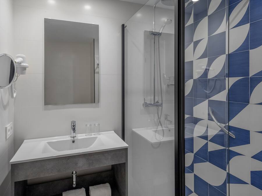 Un baño moderno con lavamanos, espejo y ducha blancos.