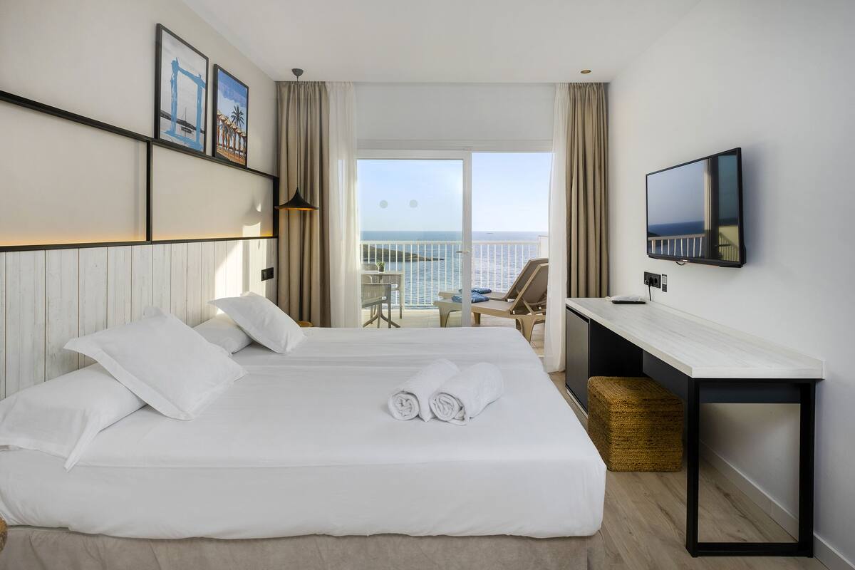 Une chambre d’hôtel avec un lit, un bureau, une télévision et un balcon donnant sur la mer.