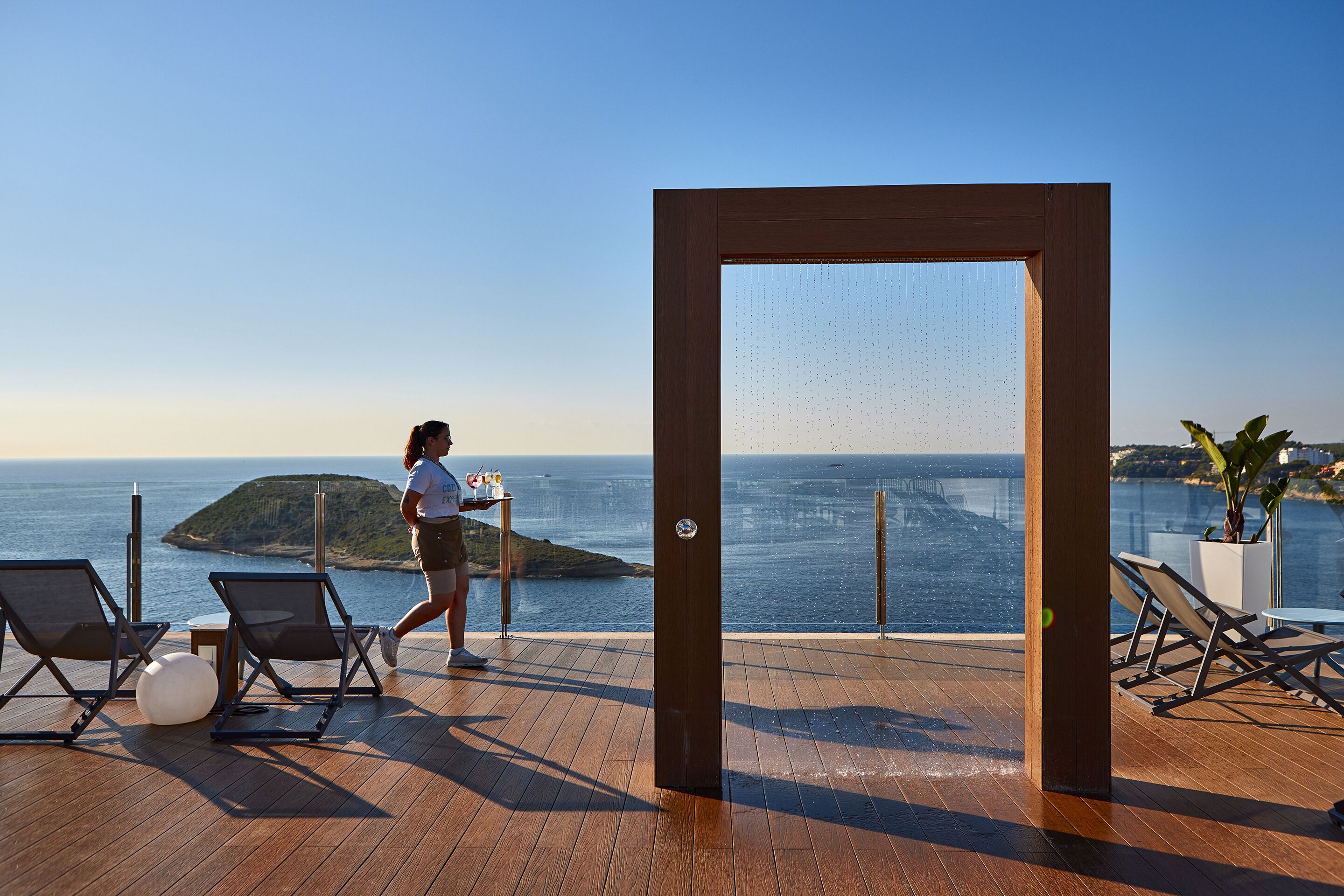 Une terrasse en bois avec des chaises longues et vue sur la mer.