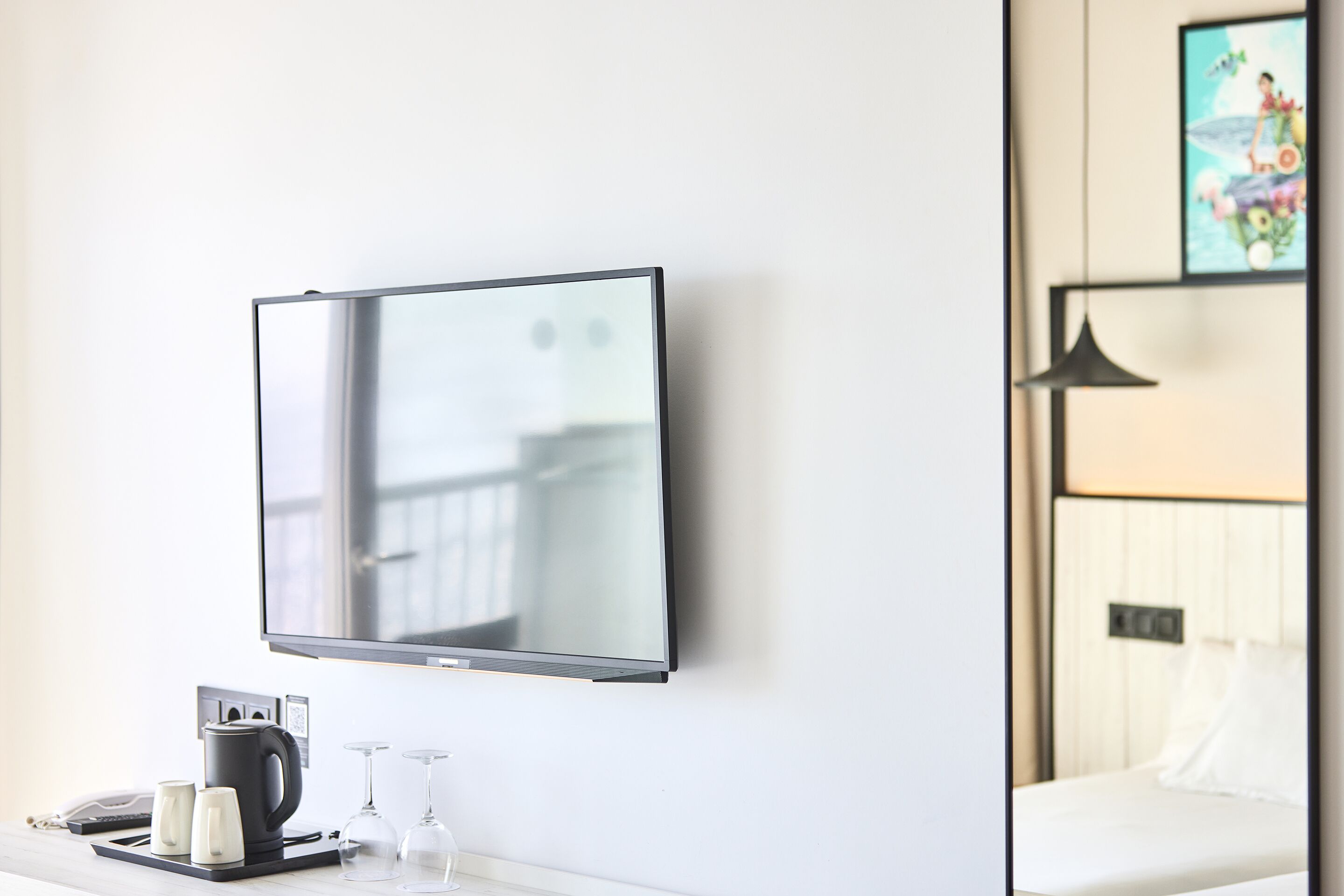 Una habitación de hotel moderna con un televisor de pantalla plana montado en la pared, una cafetera y dos copas de vino sobre una mesita auxiliar.