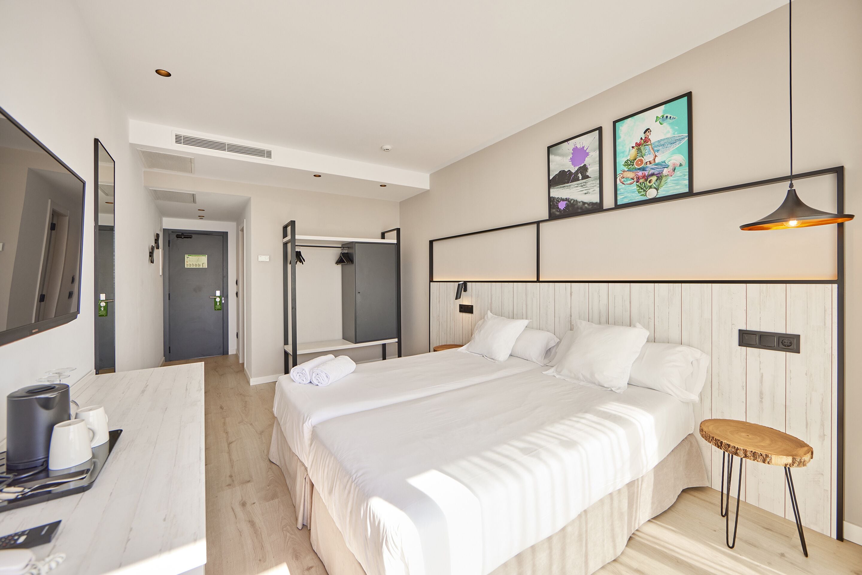 Ett modernt hotellrum med en stor säng, ett skrivbord med en kaffebryggare och konstverk på väggen.