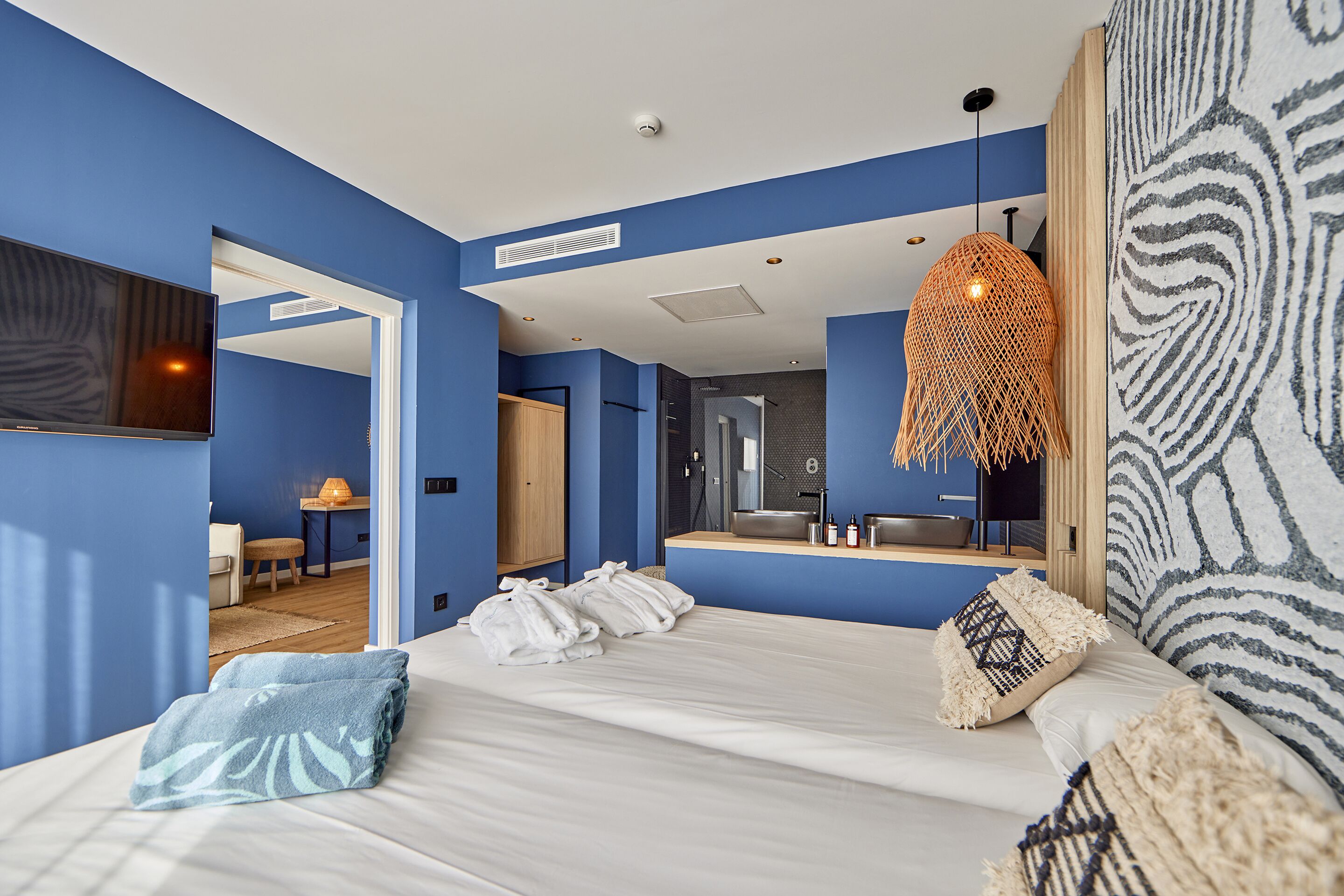 Et moderne hotelværelse med en stor seng, en hængende lampe og et badeværelse, der kan ses igennem en åben dør.