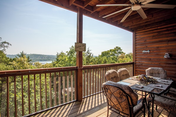 A wooden deck with a table and chairs, overlooking a lake and hills.