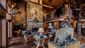 A log cabin interior with a stone wall, wooden furniture, and mounted animal heads. - The Village At Indian Point Resort (Branson)