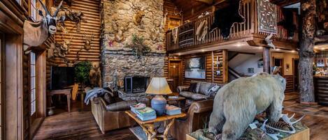 A log cabin interior with a stone wall, wooden furniture, and mounted animal heads.
