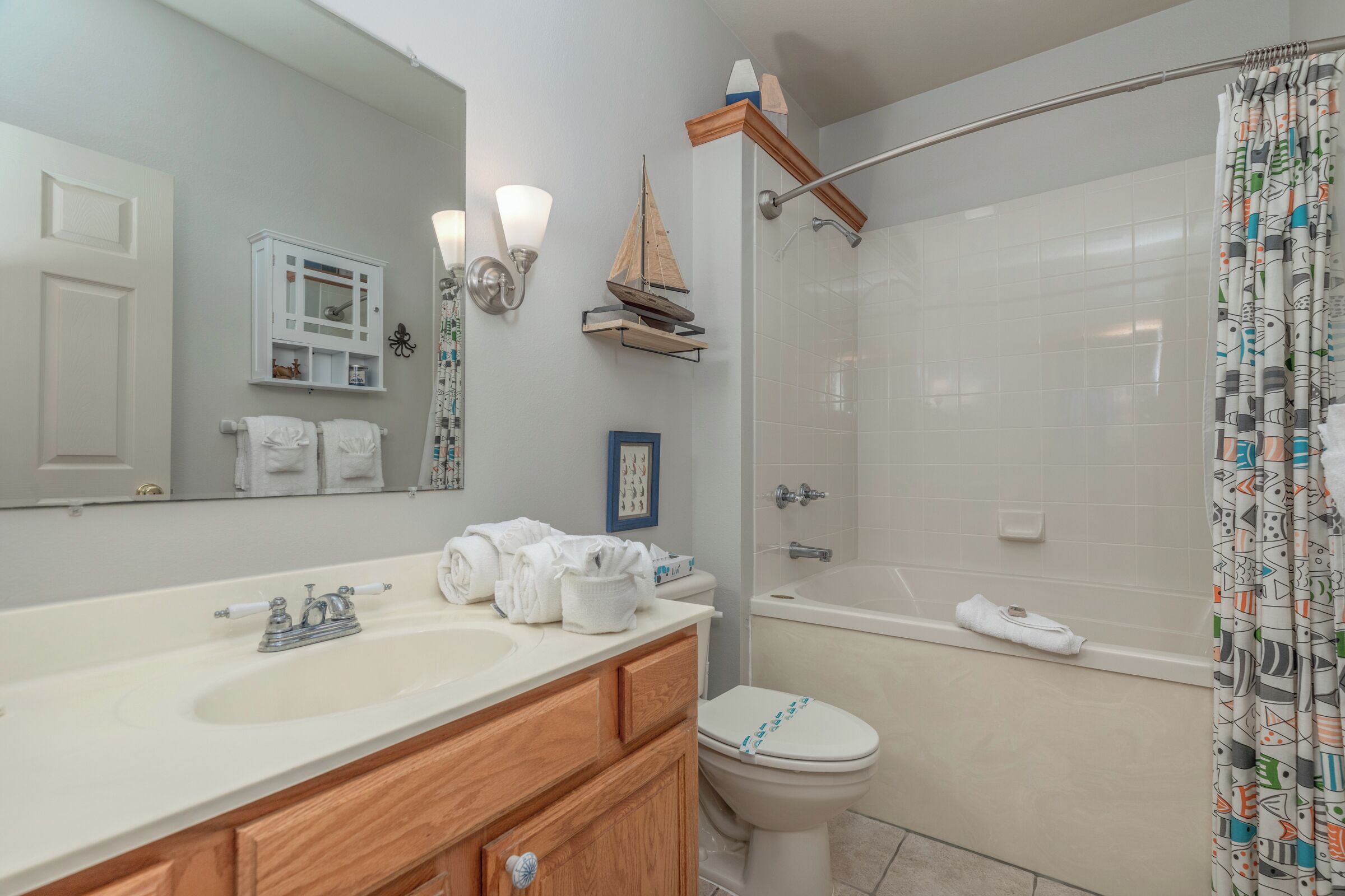 Un baño con lavamanos blanco, tocador de madera, inodoro y ducha con cortina.
