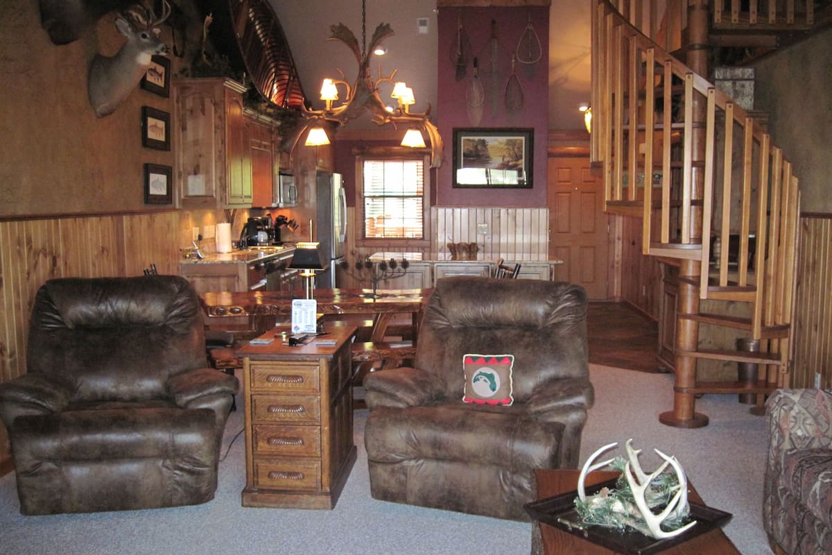 A rustic interior with leather chairs, a wooden desk, and a staircase.