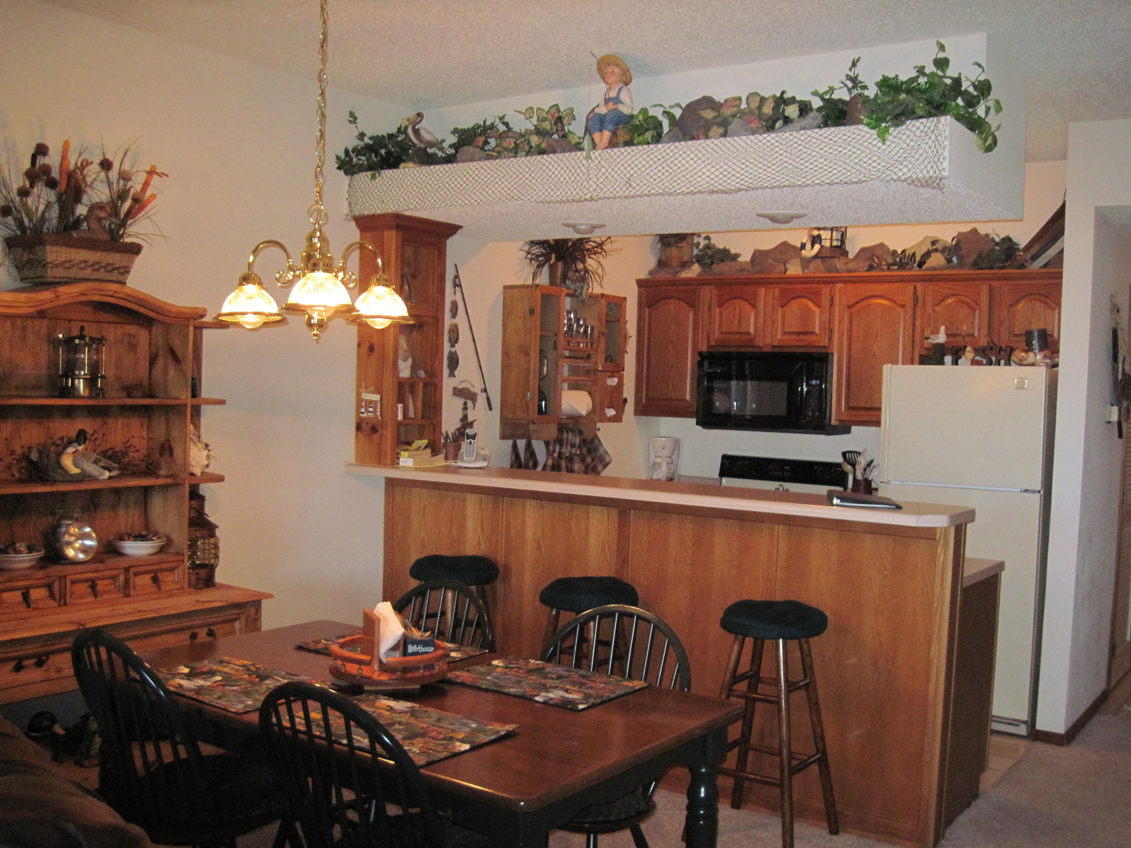A kitchen with wooden cabinets, a microwave, and a refrigerator. There is a dining table with chairs and a chandelier.