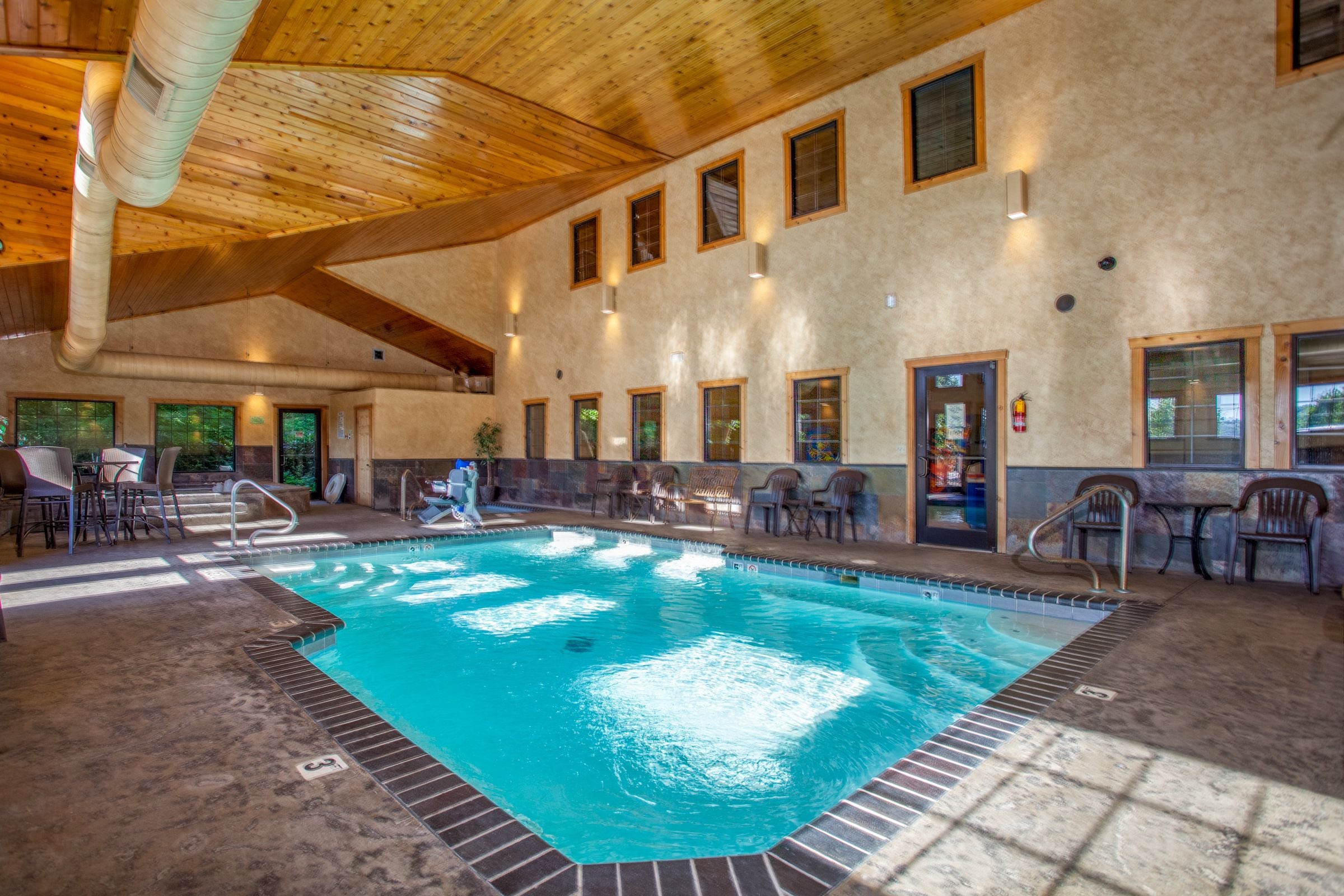 An indoor swimming pool with a wooden ceiling and multiple windows.
