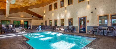 An indoor swimming pool with a wooden ceiling and multiple windows.