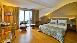 Une chambre d’hôtel avec un grand lit, un bureau avec une chaise, une petite table et une vue sur l’extérieur grâce à une porte coulissante.