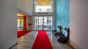 Un hall d’hôtel avec un tapis rouge, des fauteuils modernes, un grand luminaire sphérique et une enseigne indiquant « AION HOTEL ».