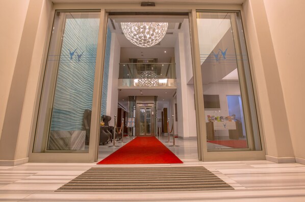 Entrada de hotel con alfombra roja, puertas dobles y un candelabro.
