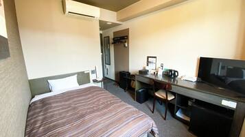 Habitación de hotel con cama, escritorio, silla, televisor y un pequeño cubo de basura.