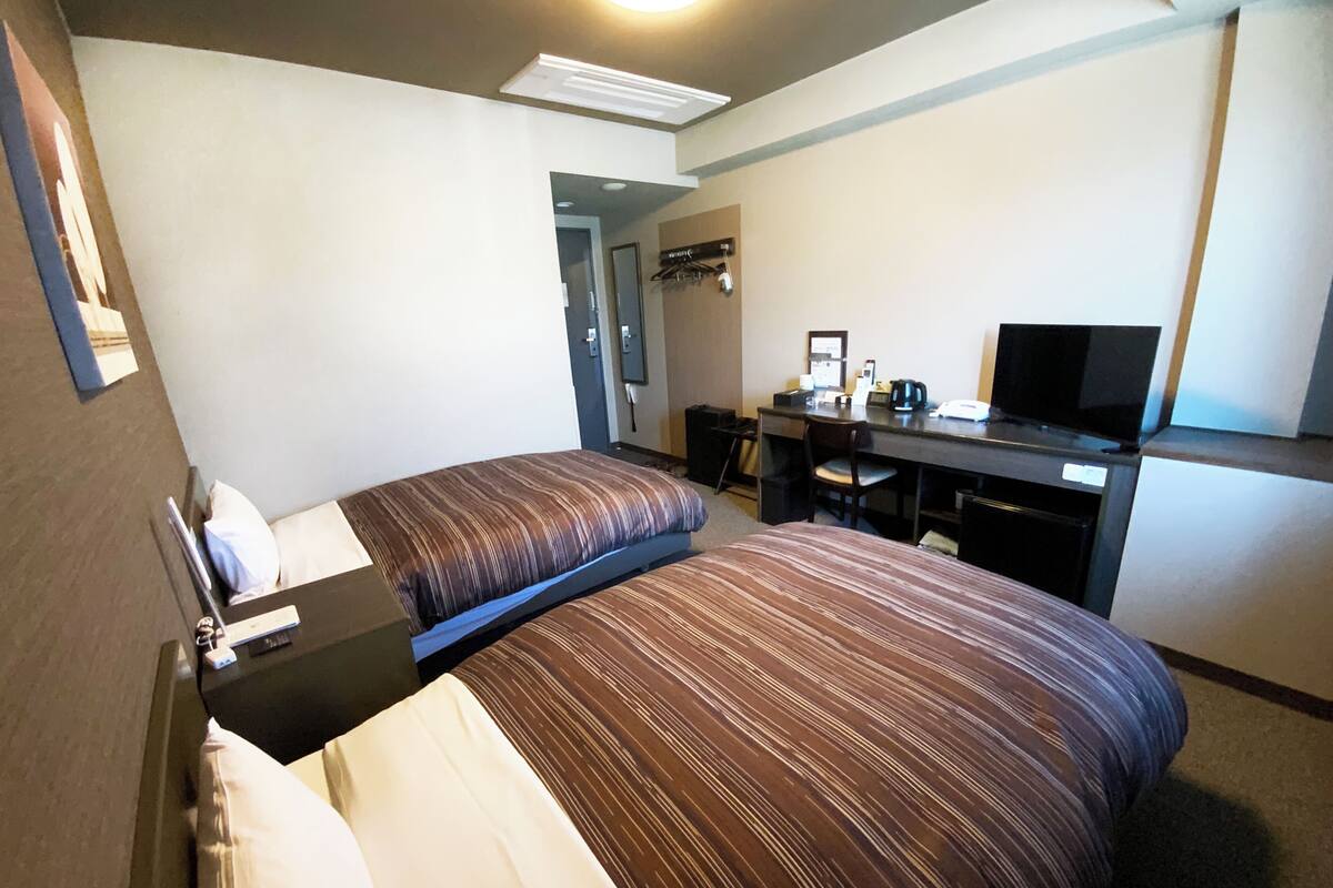 A hotel room with two beds, a desk, a chair, a television, and a mirror.