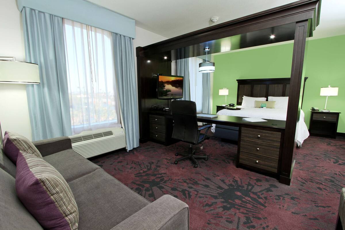 A hotel room with a bed, desk, chair, and a large mirror.