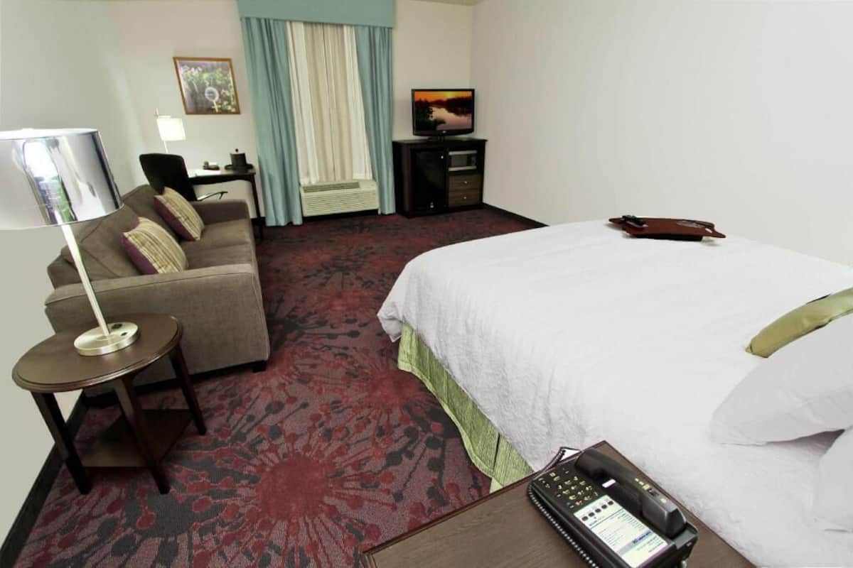 A hotel room with a bed, a desk with a lamp, a television, and a telephone.