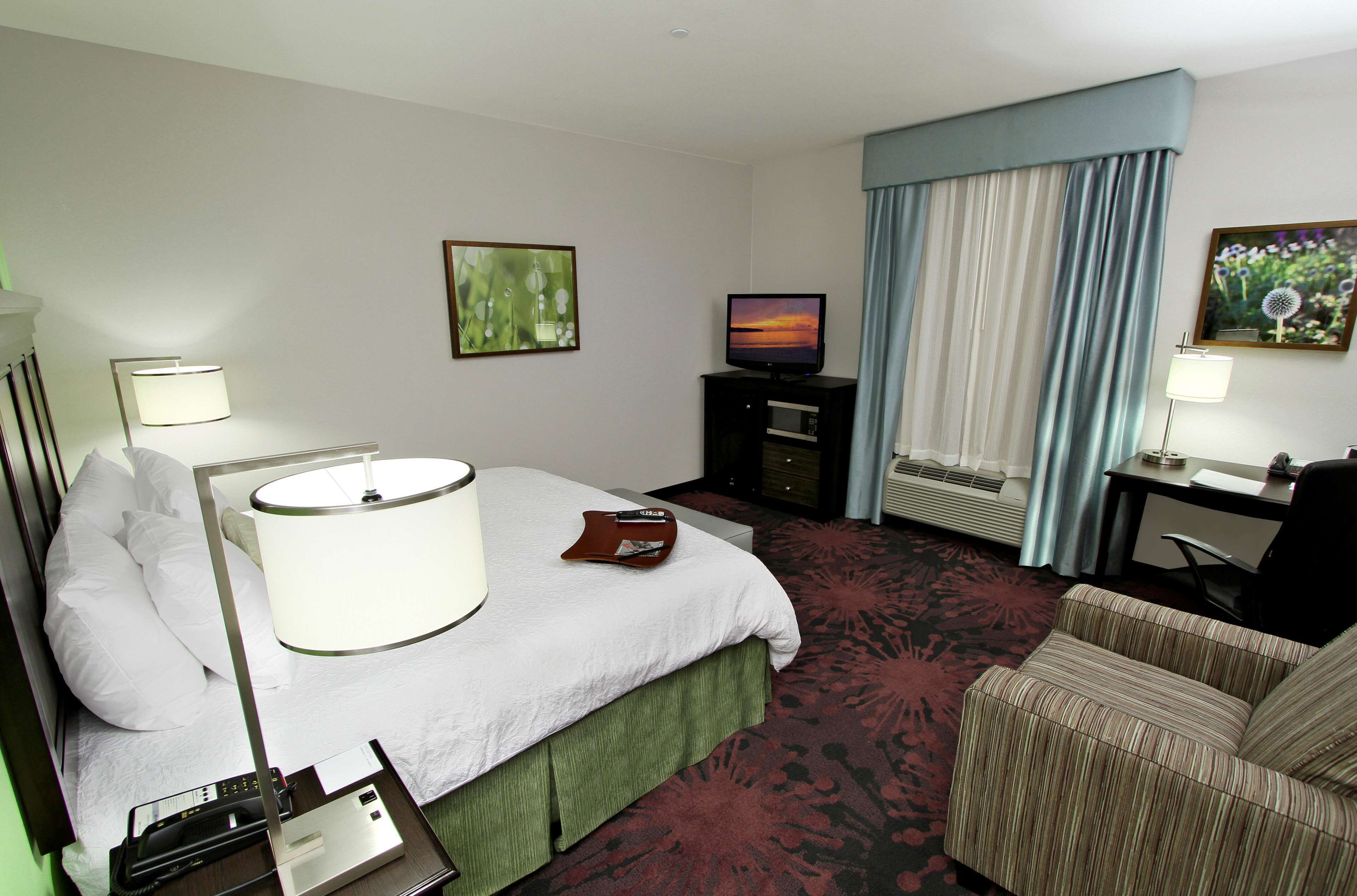 Ein Hotelzimmer mit Bett, Schreibtisch, Stuhl, Fernseher und einem Fenster mit Vorhängen.