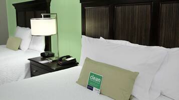 Een hotelkamer met een net opgemaakt bed, een nachtkastje met een lamp, een telefoon en een bordje dat aangeeft dat de kamer schoon is.