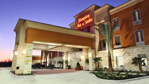 A Hampton Inn & Suites with a brick facade, a covered entrance, and palm trees.