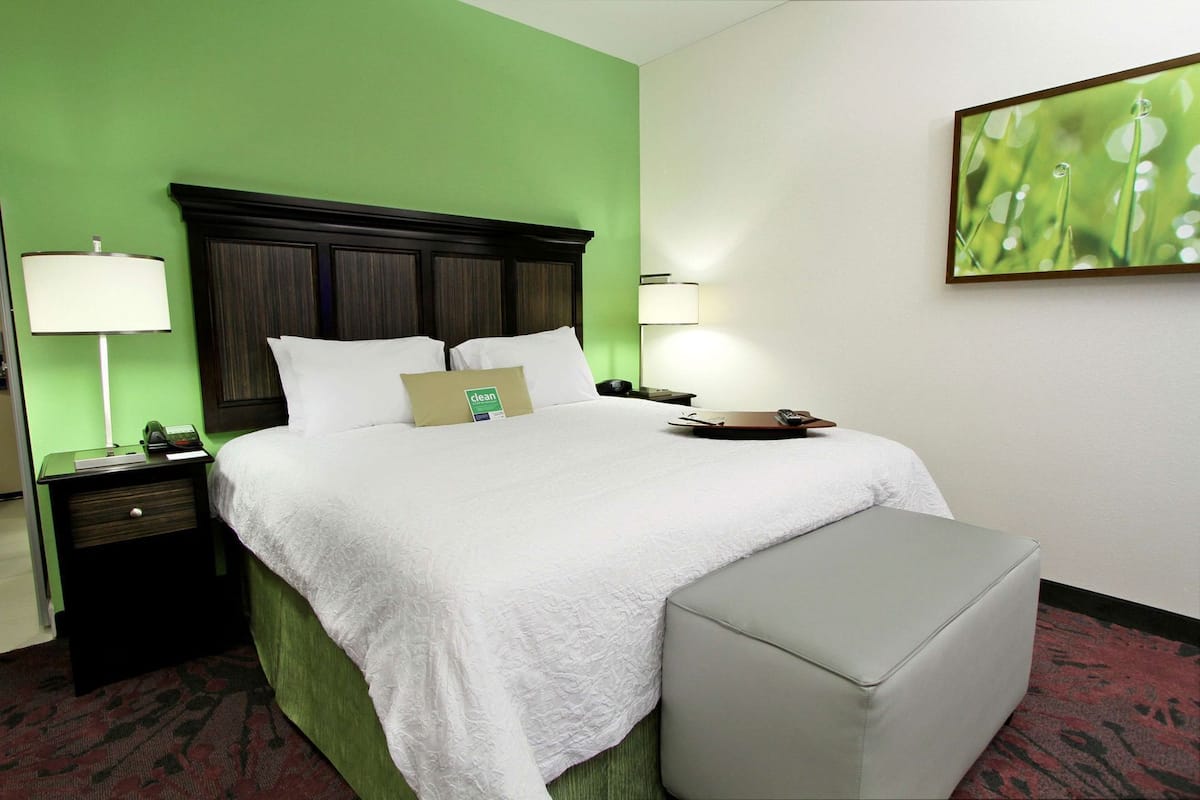 A hotel room with a bed, two bedside tables, a nightstand, a green wall, and a framed picture.