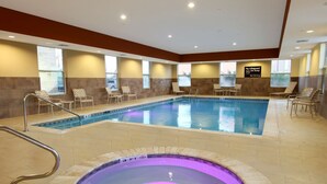 An indoor swimming pool with a hot tub, lounge chairs, and a sign indicating no lifeguard on duty.