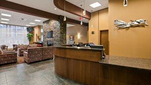 A reception area with a stone wall, a wooden reception desk, and a seating area with patterned sofas. - Best Western Plus Chateau Inn Sylvan Lake (Sylvan Lake)