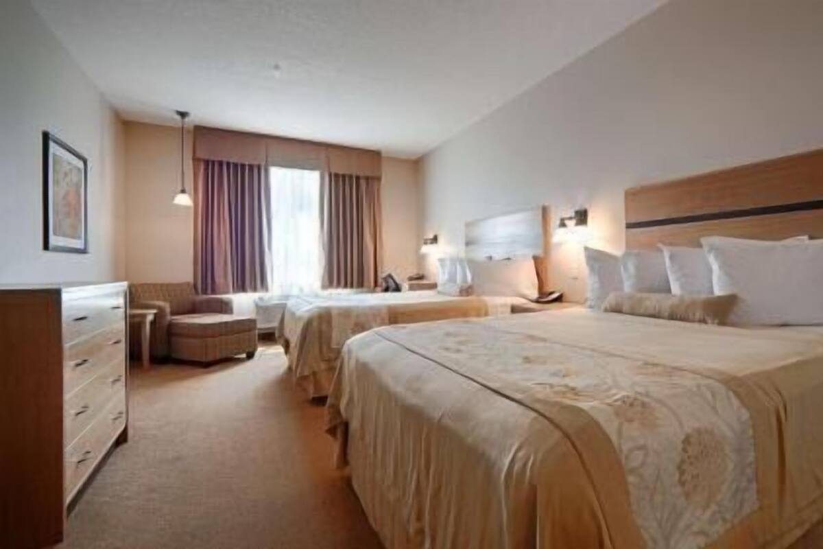 A hotel room with two beds, a dresser, a chair, and a window with curtains.