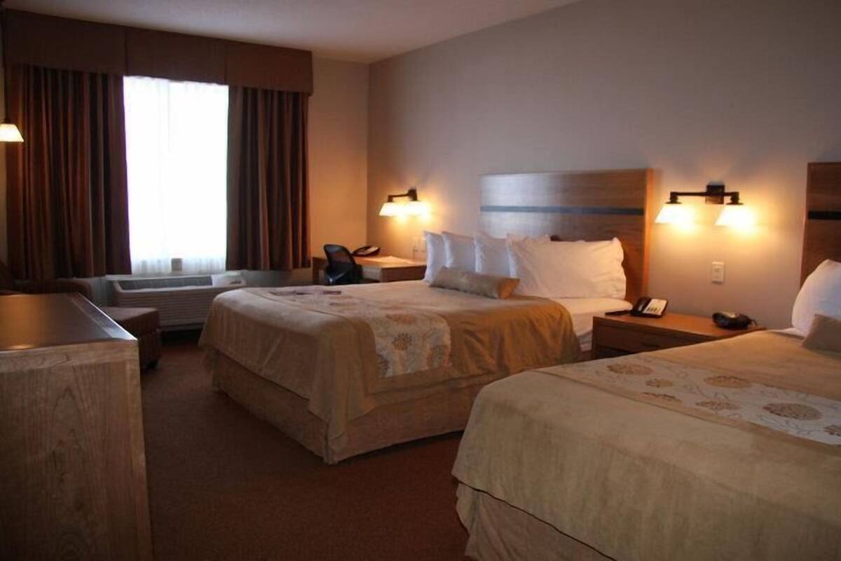 A hotel room with two beds, a desk, a chair, and a window with curtains.