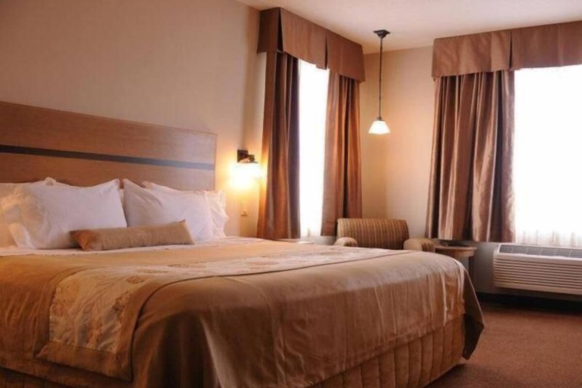 A hotel room with a large bed, a bedside table, a chair, and a window with curtains.