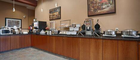 Un comptoir de buffet proposant divers aliments et appareils, notamment une machine à café, un appareil à gaufres et des distributeurs de nourriture.