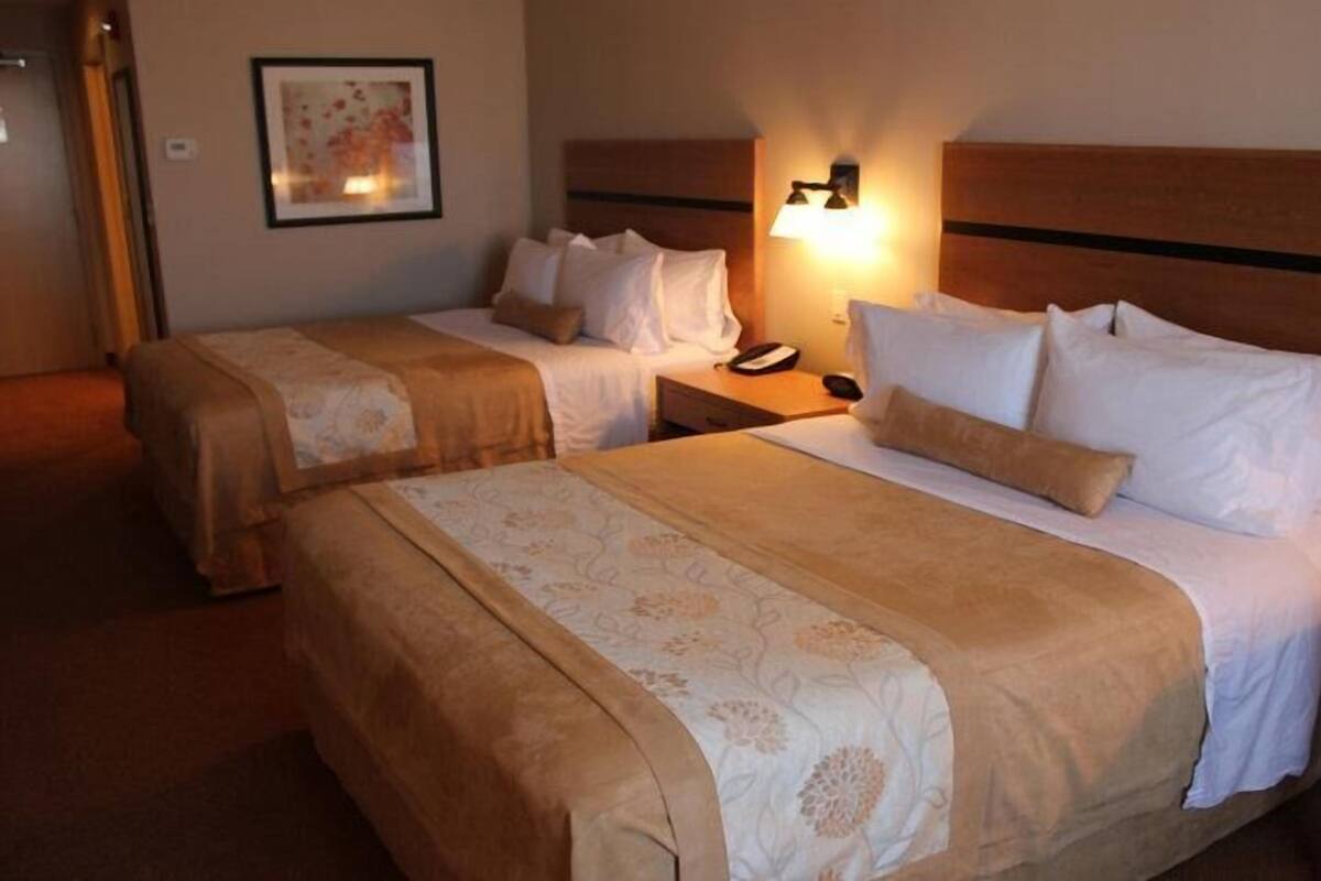 A hotel room with two beds, each with a headboard, bedside tables, and a lamp.