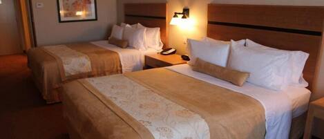 A hotel room with two beds, each with a headboard, bedside tables, and a lamp.
