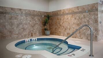 A hot tub with a metal ladder, surrounded by beige tiles and a decorative border.