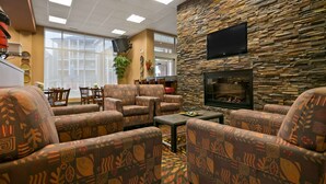A cozy lounge area with patterned sofas, a stone wall, a flat-screen TV, and a fireplace. - Best Western Plus Chateau Inn Sylvan Lake (Sylvan Lake)