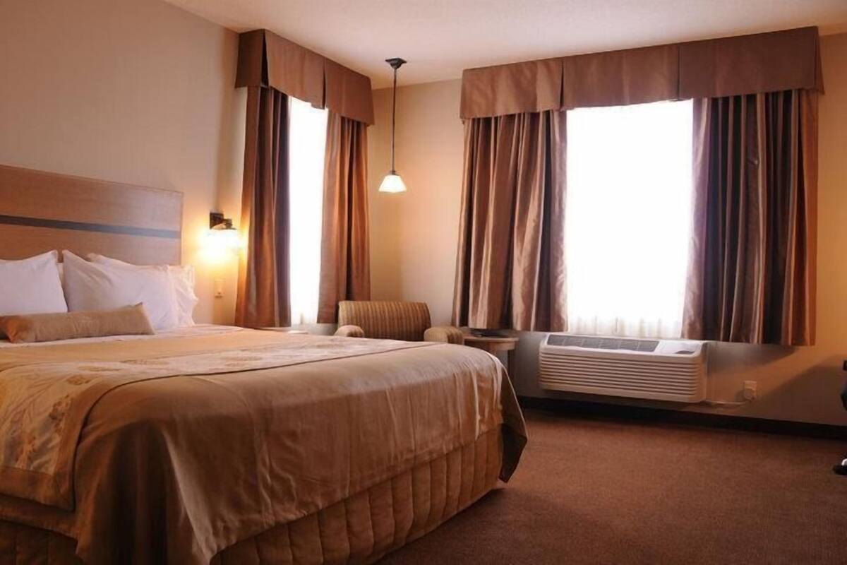 A hotel room with a large bed, a chair, a desk, and a window with curtains.