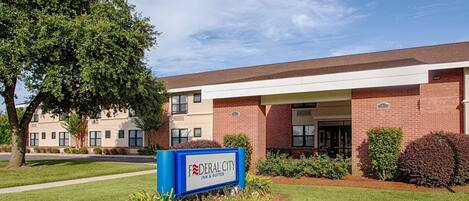 A Federal City Inn & Suites building with a brick facade, a covered entrance, and a well-maintained lawn.