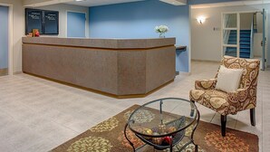 A reception area with a reception desk, a chair, a glass table with decorative items, and a patterned rug. - Federal City Inn & Suites (New Orleans)