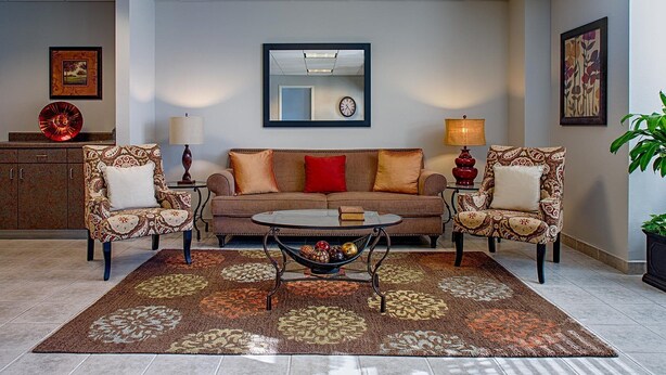 A living room with a brown sofa, patterned armchairs, a coffee table, and a decorative rug. - Federal City Inn & Suites (New Orleans)