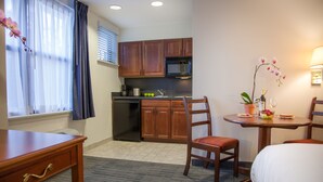 A hotel room with a kitchenette, a dining table with chairs, a bed, and a window with curtains. - Federal City Inn & Suites (New Orleans)