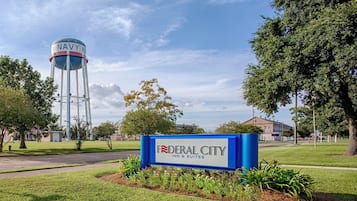 Um letreiro de hotel com a inscrição 'Federal City Inn & Suites' e uma torre d'água com a inscrição 'NAVY N' ao fundo.