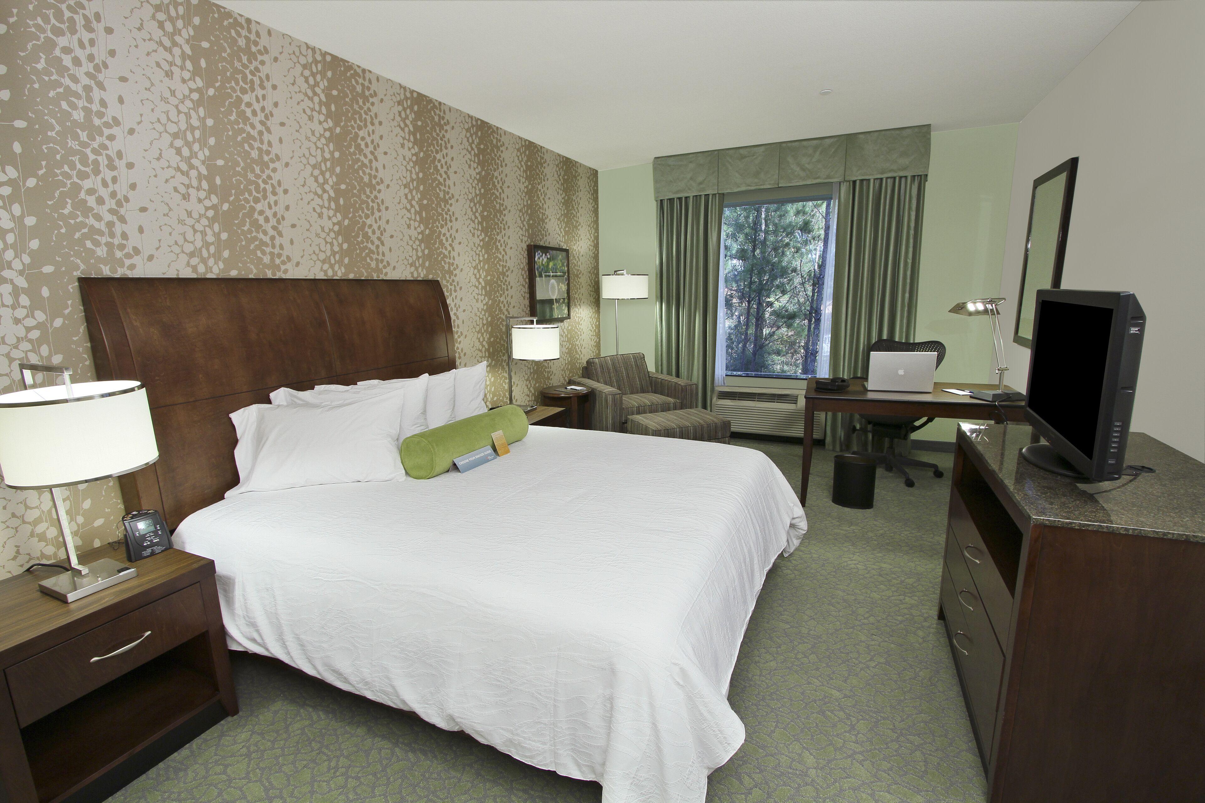 Une chambre d’hôtel avec un grand lit, un bureau avec un ordinateur, une chaise, une télévision et une fenêtre avec des rideaux.