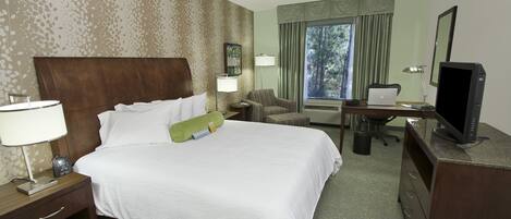 Une chambre d’hôtel avec un grand lit, un bureau avec un ordinateur, une chaise, une télévision et une fenêtre avec des rideaux.