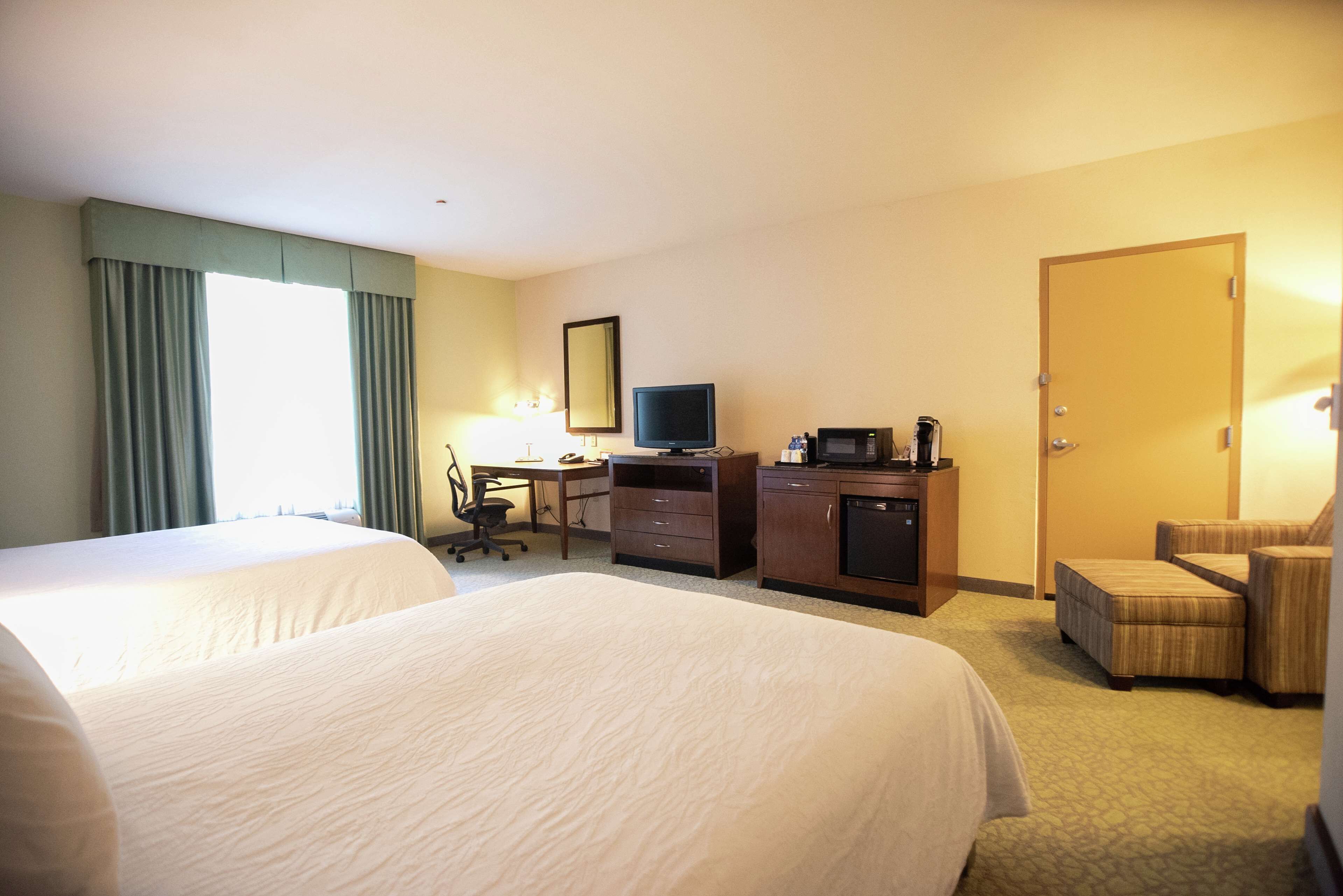 A hotel room with two large beds, a desk with a computer, a television, a coffee maker, and a chair.